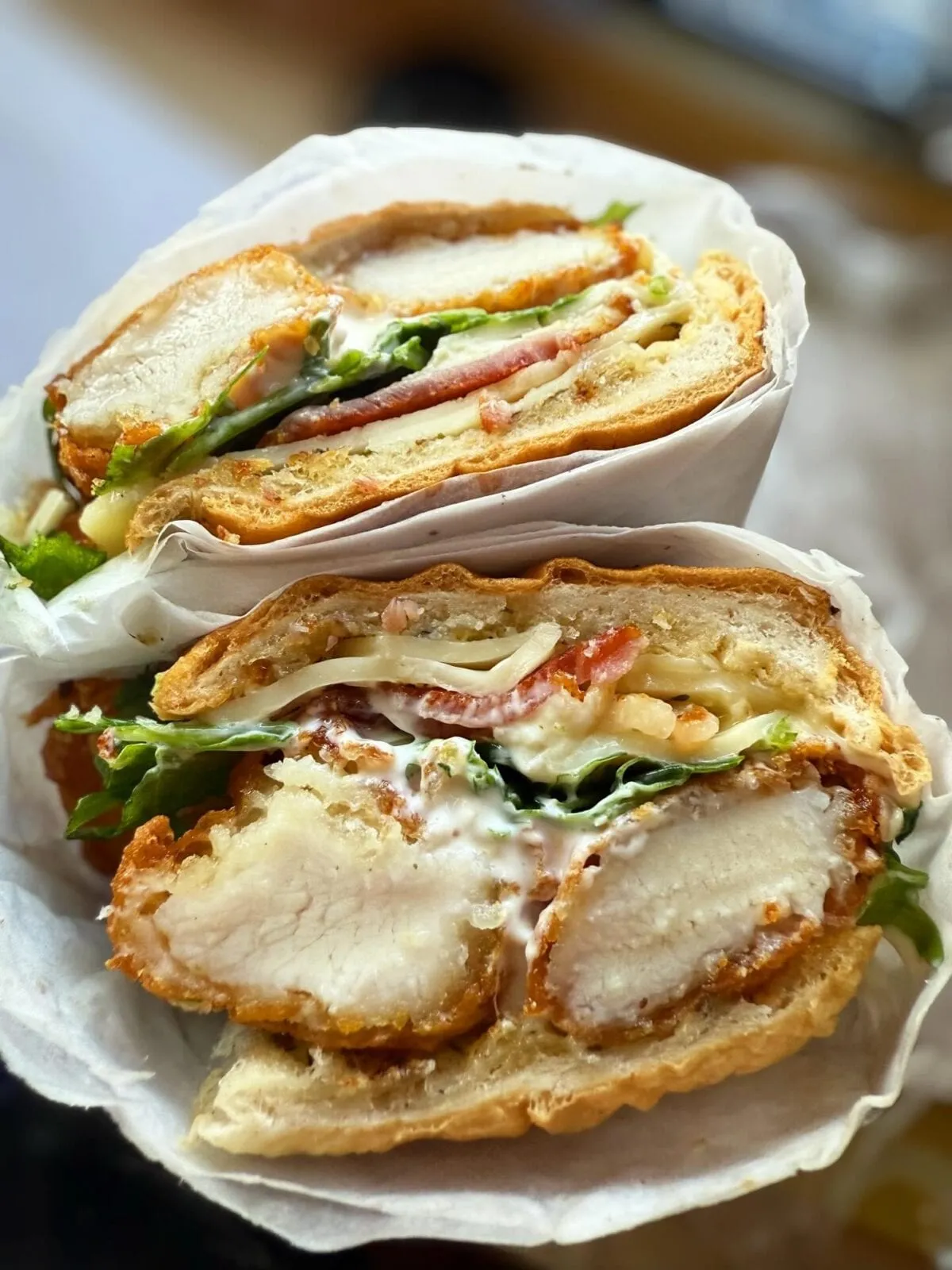 A freshly-cut loaded chicken and bacon bagel from Crumbs & Grind — crispy chicken, melted cheese, and fresh salad — wrapped and ready to share on social